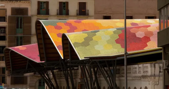 A wavy roof covered in colorful mosaic above a market building, against residential houses