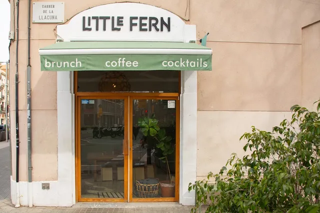 A corner storefront with a green awning, glazed wooden doors and a green shrub at the side
