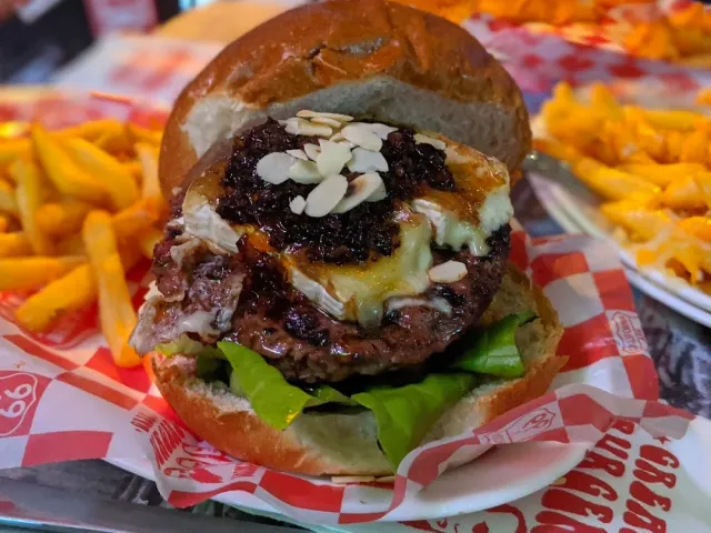 A tall burger with cheese and dark sauce, in a checkered paper basket beside fries