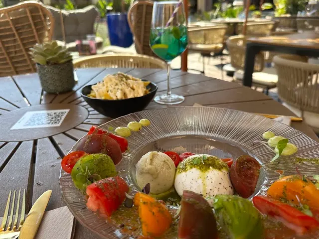 A plate with white cheese balls, colorful tomatoes and green oil, on an outdoor table