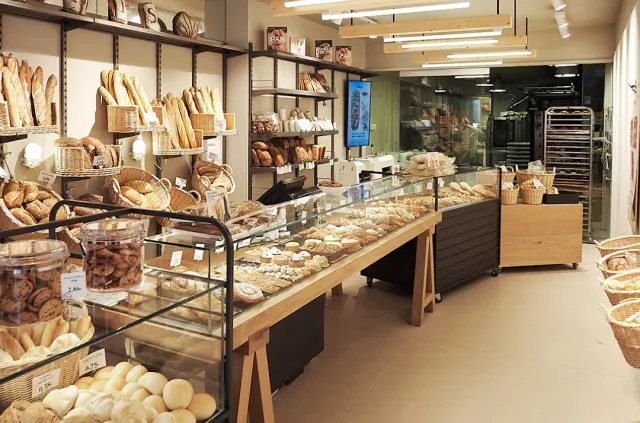 A bread shop with loaves in baskets and on shelves, and a long display counter in the middle