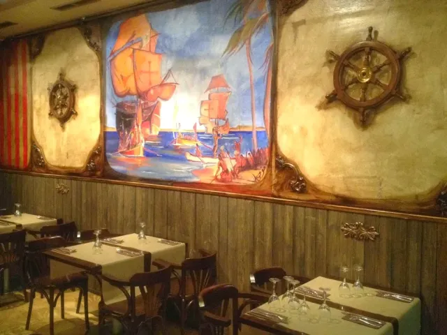 A hall with a wall painting of sailing ships, a wooden helm and wood panelling below
