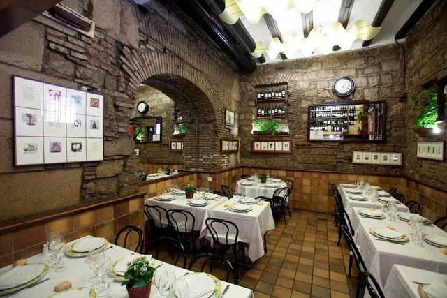 A dining room with stone walls and an arch, tables in white cloths and framed pictures
