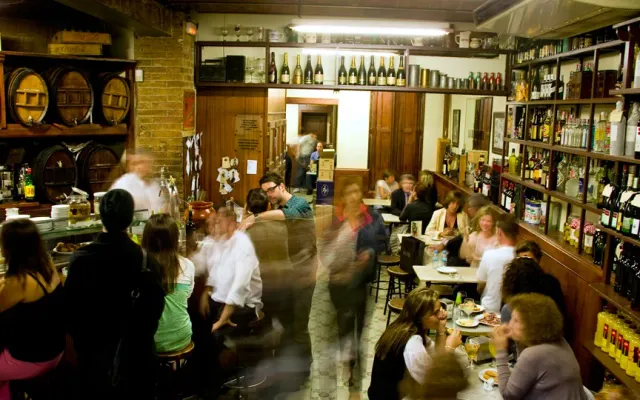 A crowded cellar with wooden barrels, shelves of bottles and diners blurred in motion
