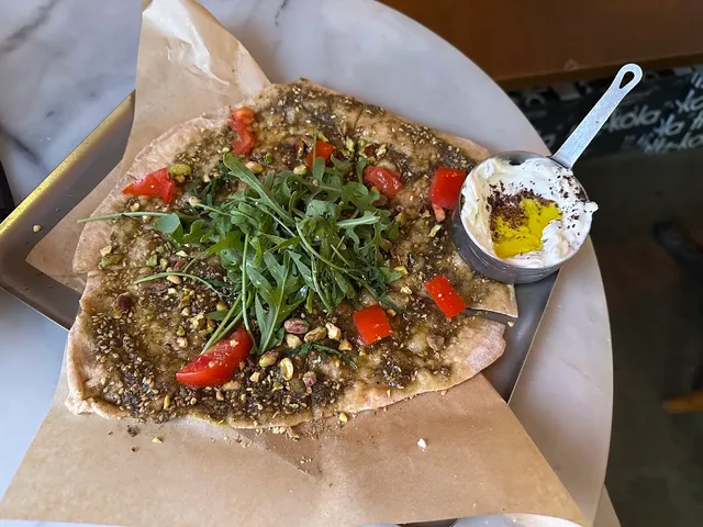 A flatbread with za'atar, rocket and tomatoes, beside a small pot of labneh