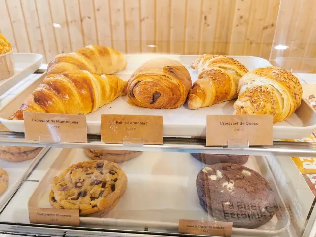 A display case with croissants and cookies on trays, and price labels in front of each item