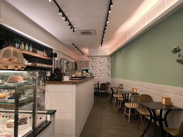 A long bright space with a white counter, a cake display and small tables along a green wall