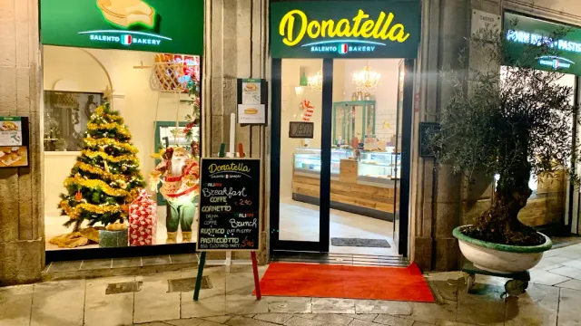 A facade lit in the evening with a green sign, a decorated tree in the window and a red carpet at the door