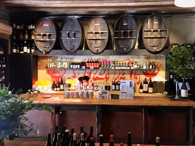 A wooden counter facing large wine barrels and shelves full of bottles