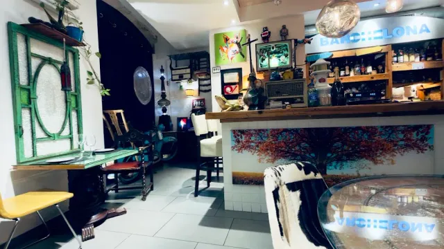 A colorful bar interior with a green window frame on the wall, mixed furniture and a painted counter