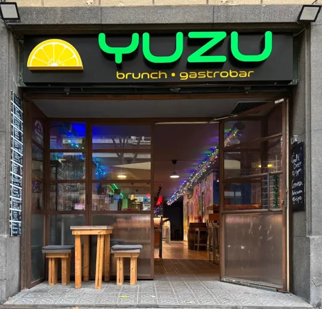 An open storefront with a green neon sign, wooden stools and chalkboards on both sides