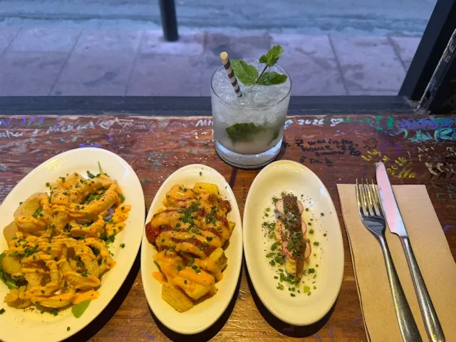 Three small dishes on a wooden table covered in writing, with a glass of drink and mint