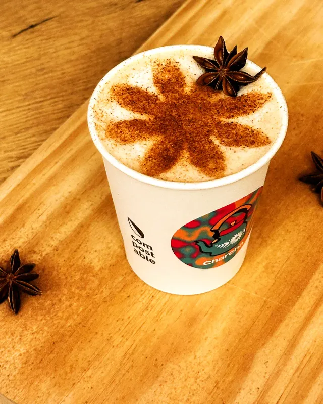 A paper cup with foam dusted in cinnamon in a flower shape and a star anise, on wood