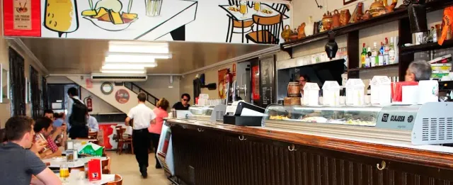A long counter with a chilled display case, a wall drawing above and tables on the left