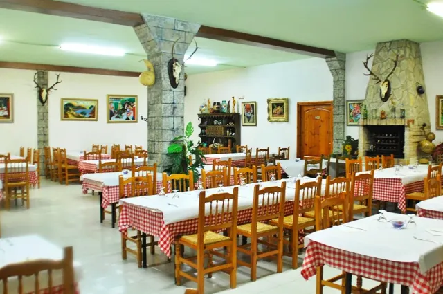 A wide hall with red checked cloths, wicker chairs and a stone fireplace at the end