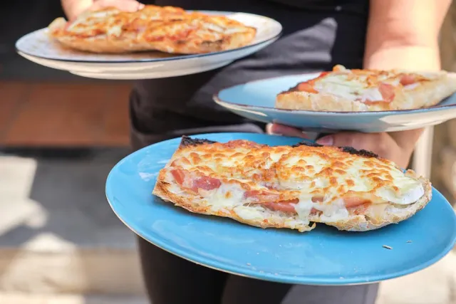 Hands holding three light blue plates with loaves baked in melted cheese