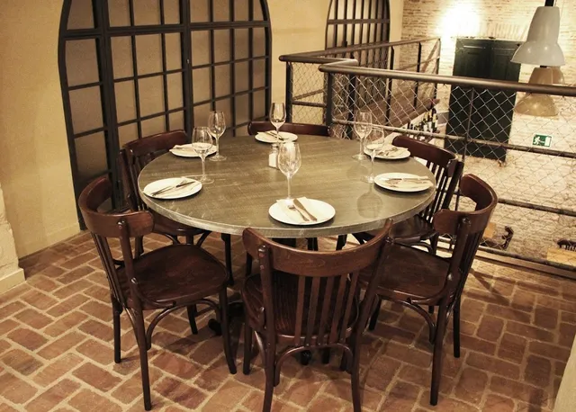 A round set table with dark wooden chairs on a brick floor, beside a mesh railing