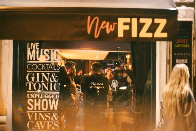 A lit bar entrance in the evening, with people inside and cocktail signs on the wall