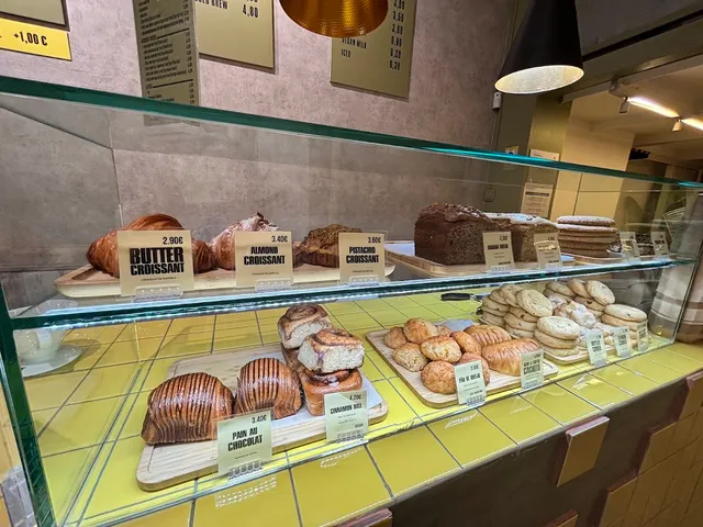 A glass display case with croissants, loaves and pastries on a yellow tiled counter