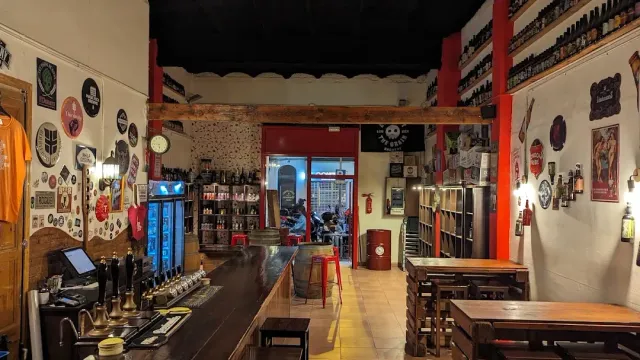 A wooden bar with taps, walls covered in beer labels and wooden tables beyond