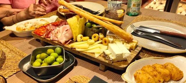 A wooden board with cheeses, cured meats and olives, and a bowl of green olives beside it