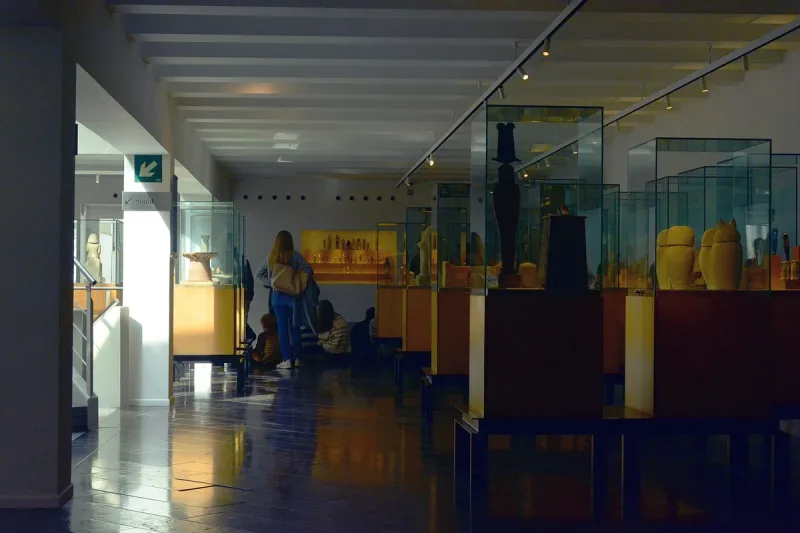 Museum hall with glass cases holding Egyptian vessels and statues