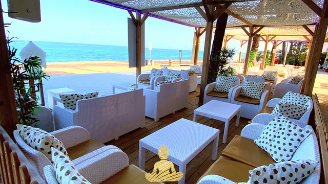 White wicker sofas with dotted cushions under a pergola, facing the sea
