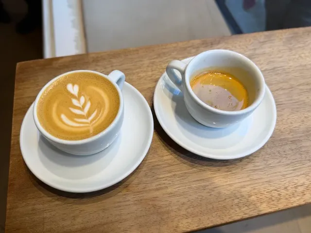 Two white cups on saucers on a wooden counter, one with foam art