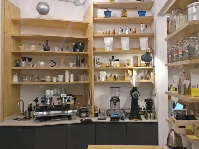 A coffee station with an espresso machine, a grinder and wooden shelves loaded with cups and jars