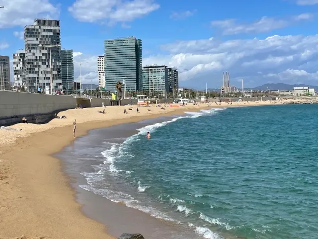Small waves breaking on wet sand, and glass towers at the end of the promenade