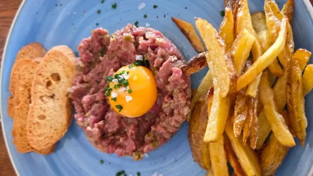 Raw minced meat with an egg yolk at the center, fried potatoes and toasted bread