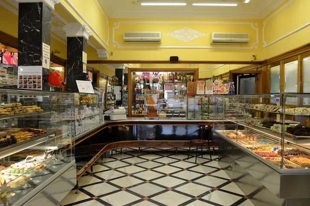 A shop with yellow walls, a checkered floor and display cases full of biscuits and sweets