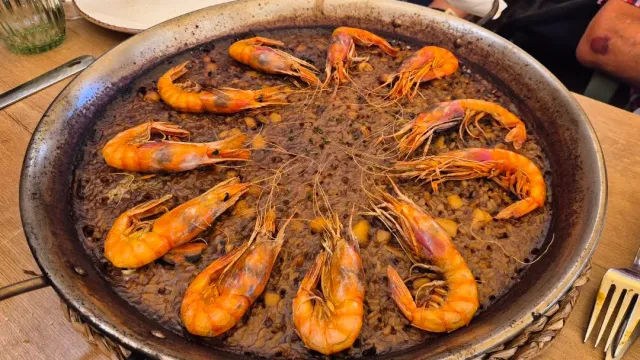 A wide rice pan with prawns arranged in a circle, on a wooden table