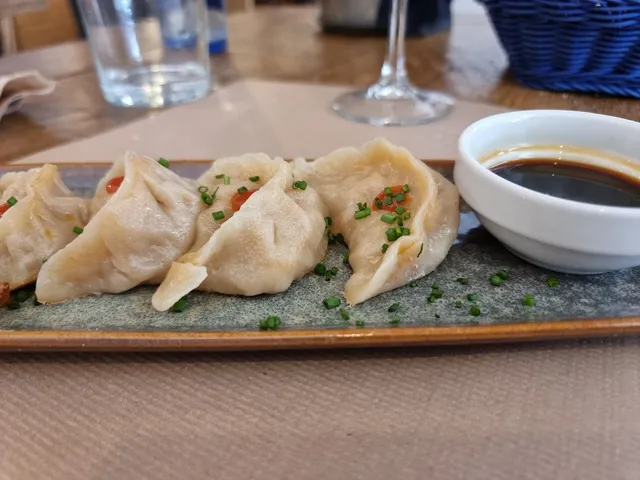 Steamed dumplings with chives on a tray, beside a small bowl of soy sauce