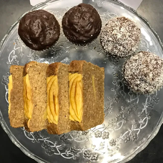 A decorated glass plate with chocolate balls, coconut balls and slices of pastry with yellow filling