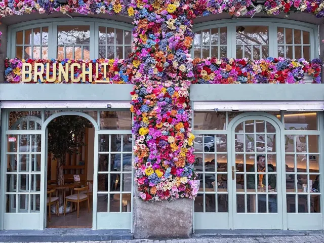 A pale green facade with a pillar covered entirely in colorful flowers and a gold lettered sign