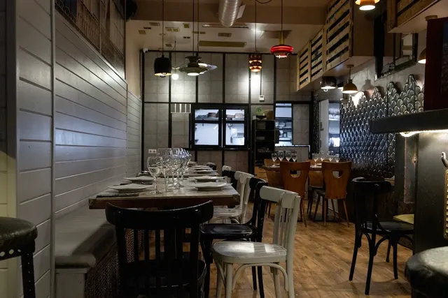 A narrow, intimate room with a long set table, wooden chairs and hanging lamps