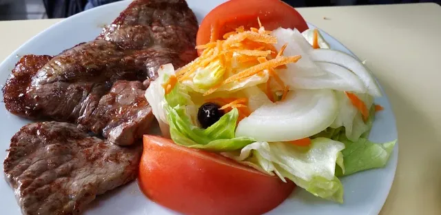 Two slices of grilled meat on a white plate beside a salad of tomato, onion and carrot