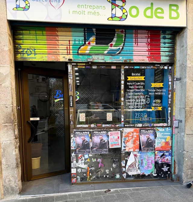 A small frontage with a painted shutter, a sandwich menu in the window and posters stuck on