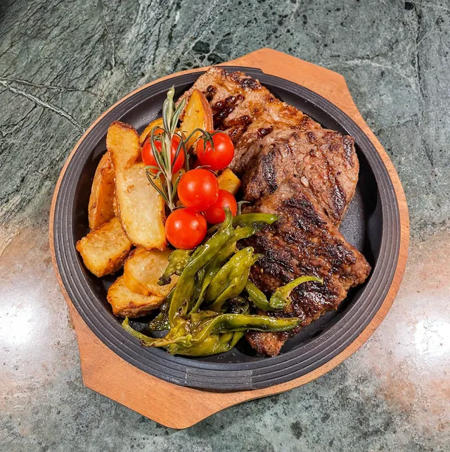 A grilled steak in an iron pan with potatoes, cherry tomatoes and green peppers