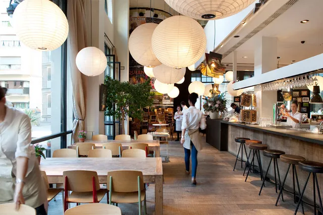 A tall room with large round paper lamps, long wooden tables and a bar along the side