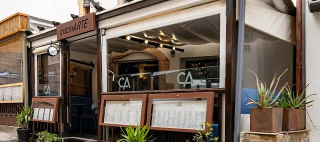 A glazed front with a pale awning, menu boards and cactus pots at the entrance