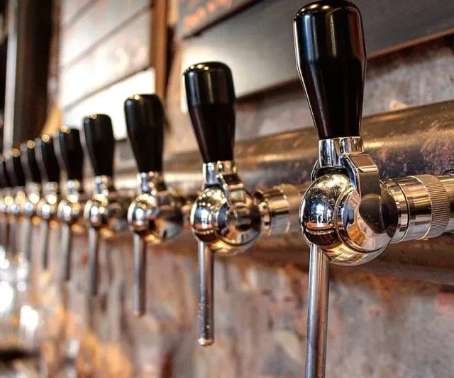 A row of chrome beer taps with black handles, in close up along the counter