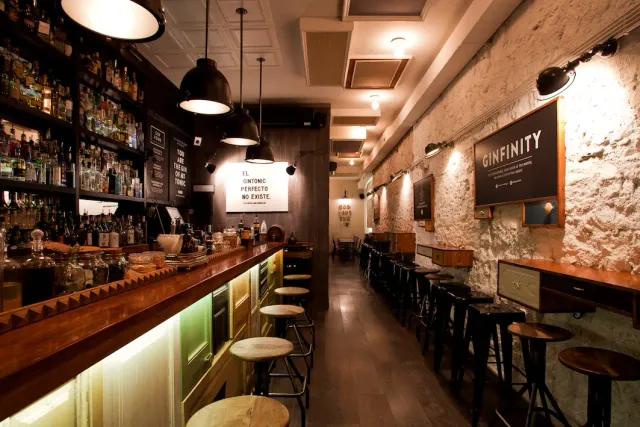 A long wooden bar with stools, bottle shelves along the wall and hanging lamps