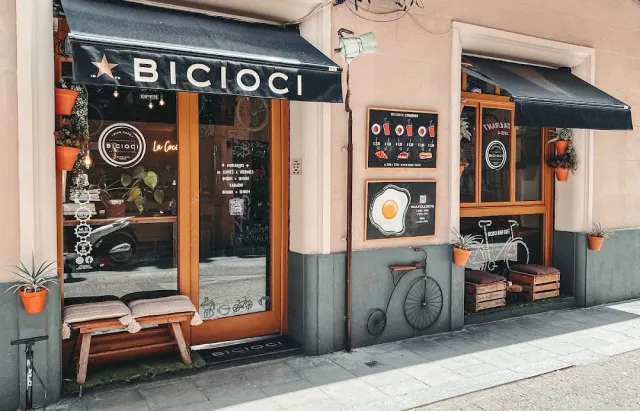 A facade with dark awnings, a decorative penny farthing bicycle and a wooden bench at the entrance