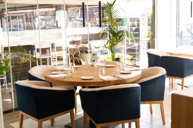 A round wooden table set with blue velvet armchairs and glass walls around