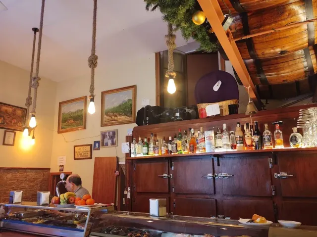 A bar interior with a dark wooden counter, bulbs hanging on ropes and a food display case in front