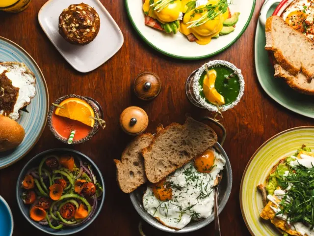 An overhead view of a wooden table loaded with plates of eggs, bread, salad and drinks