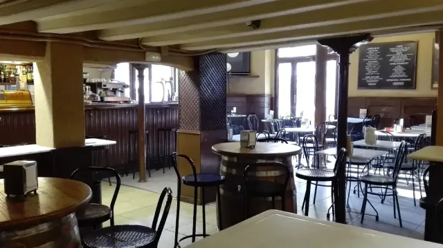 The inside of an old place with barrels as tables, iron chairs and a black menu board