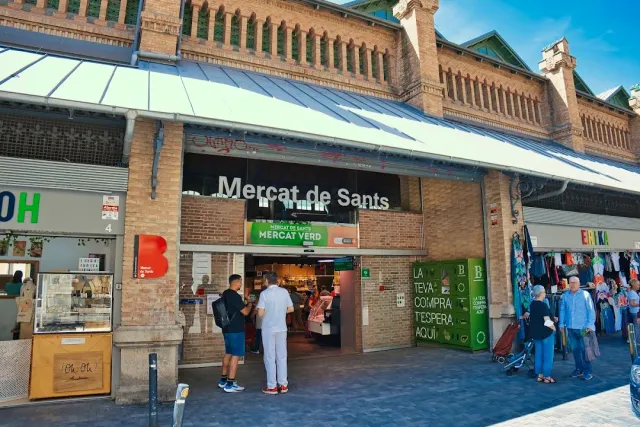 A market entrance in a red brick facade with a canopy, shoppers at the doorway and a clothing stall to the side